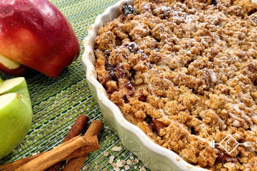 Κομμάτι μηλόπιτας με χρυσαφένια επικάλυψη crumble, γέμιση με καραμελωμένα μήλα και καρύδια σε λευκό πιάτο
