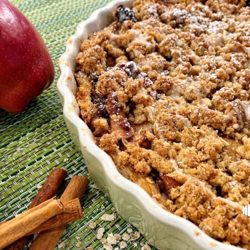 Κομμάτι μηλόπιτας με χρυσαφένια επικάλυψη crumble, γέμιση με καραμελωμένα μήλα και καρύδια σε λευκό πιάτο