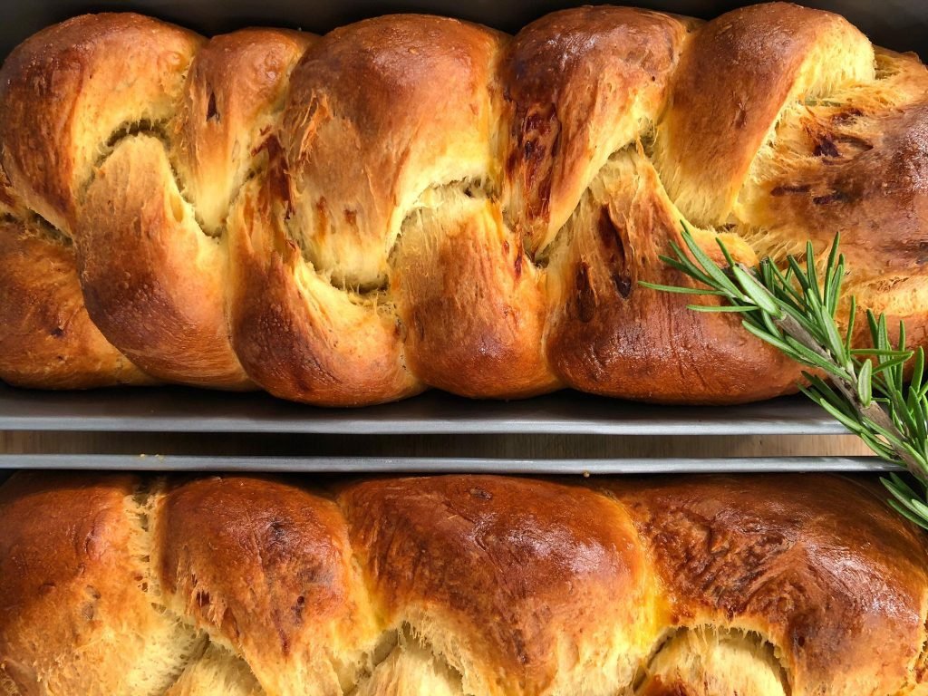 Χρυσαφένιο αλμυρό brioche πλεγμένο σε κοτσίδα με γραβιέρα και δενδρολίβανο, κομμένο σε φέτες που αποκαλύπτουν την αφράτη υφή