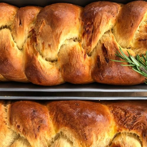 Χρυσαφένιο αλμυρό brioche πλεγμένο σε κοτσίδα με γραβιέρα και δενδρολίβανο, κομμένο σε φέτες που αποκαλύπτουν την αφράτη υφή