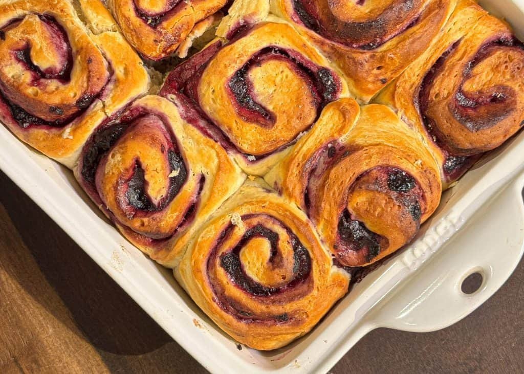 Γλυκά ρολά με μαρμελάδα blueberries και λευκό frosting τυριού κρέμα, τοποθετημένα σε ταψί, με χρυσαφένιο χρώμα ψησίματος