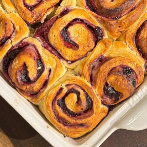 Γλυκά ρολά με μαρμελάδα blueberries και λευκό frosting τυριού κρέμα, τοποθετημένα σε ταψί, με χρυσαφένιο χρώμα ψησίματος