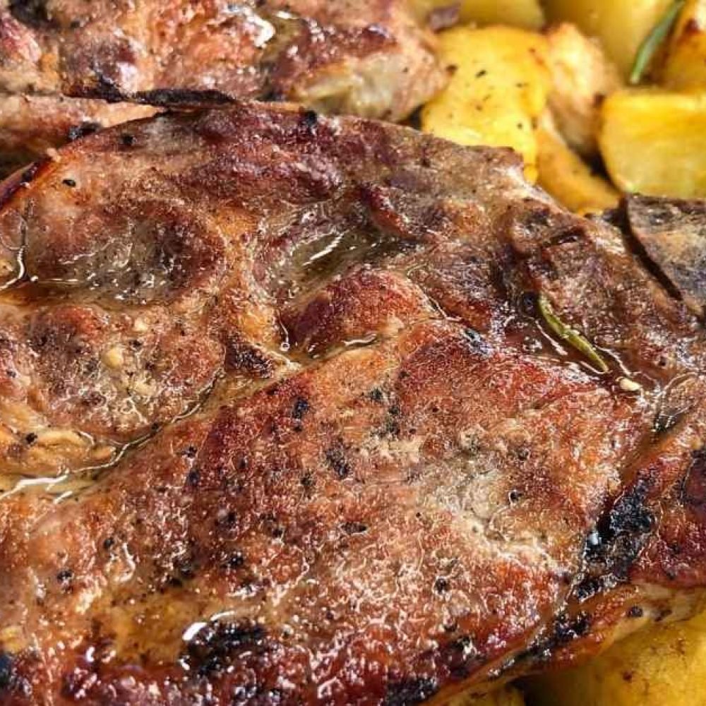 Ζουμερές χοιρινές μπριζόλες σε πιάτο με ψητές πατάτες